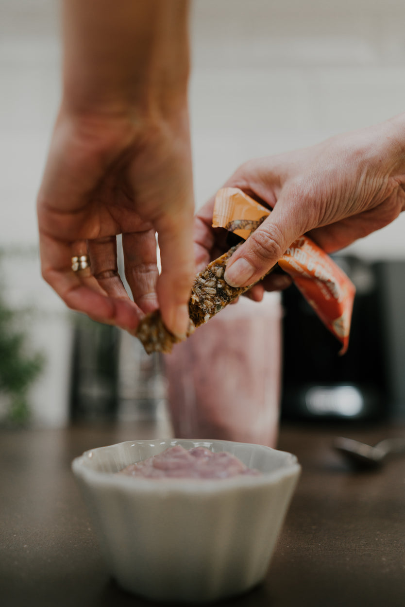 Image of a Veloforte Oat Snack Bar being added as a topper to a yoghurt for a high fibre breakfast