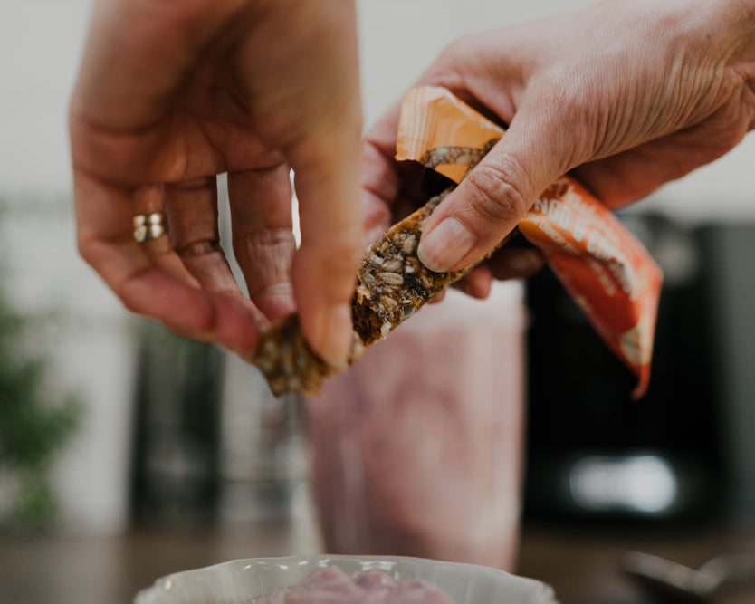 Image of a Veloforte Oat Snack Bar being added as a topper to a yoghurt for a high fibre breakfast