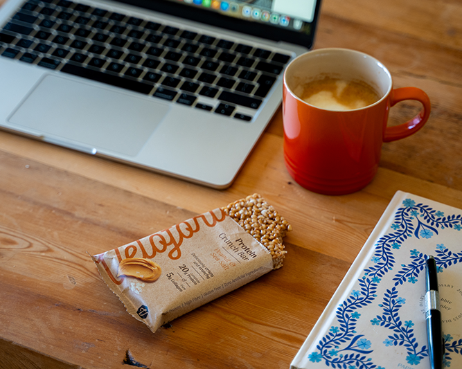protein bar on a desk next to a laptop and cup of tea