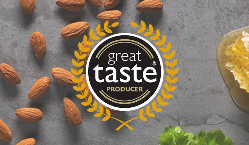 Almonds on a gray surface with 'Great Taste Producer' logo.