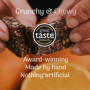 Hand holding orange and cocoa oat bar with 'great taste producer' logo and text about product quality.
