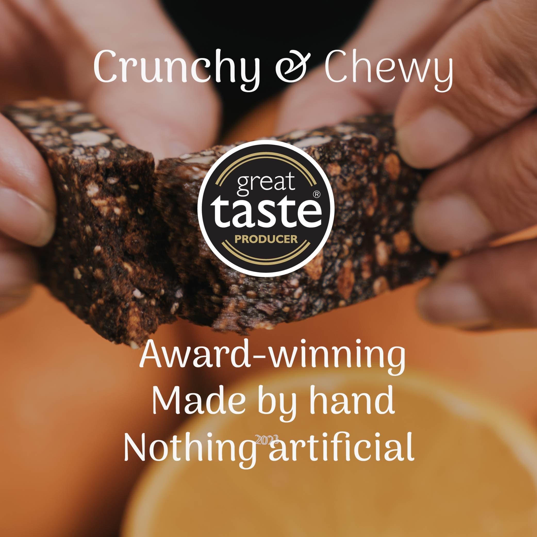 Hand holding orange and cocoa oat bar with 'great taste producer' logo and text about product quality.