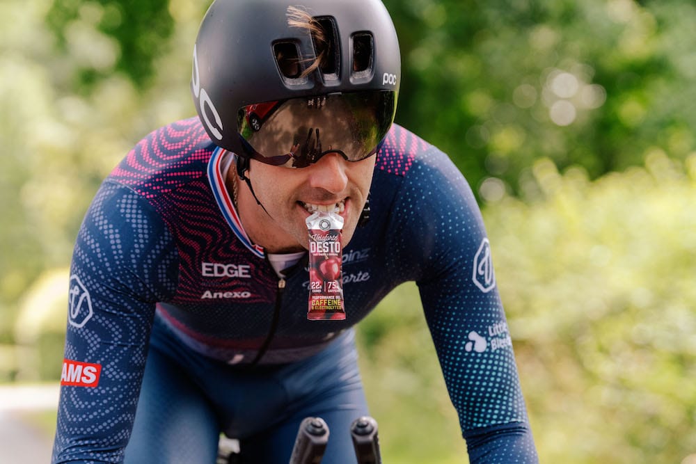 Pro cyclist on his bike with Veloforte Desto Energy Gel in his mouth