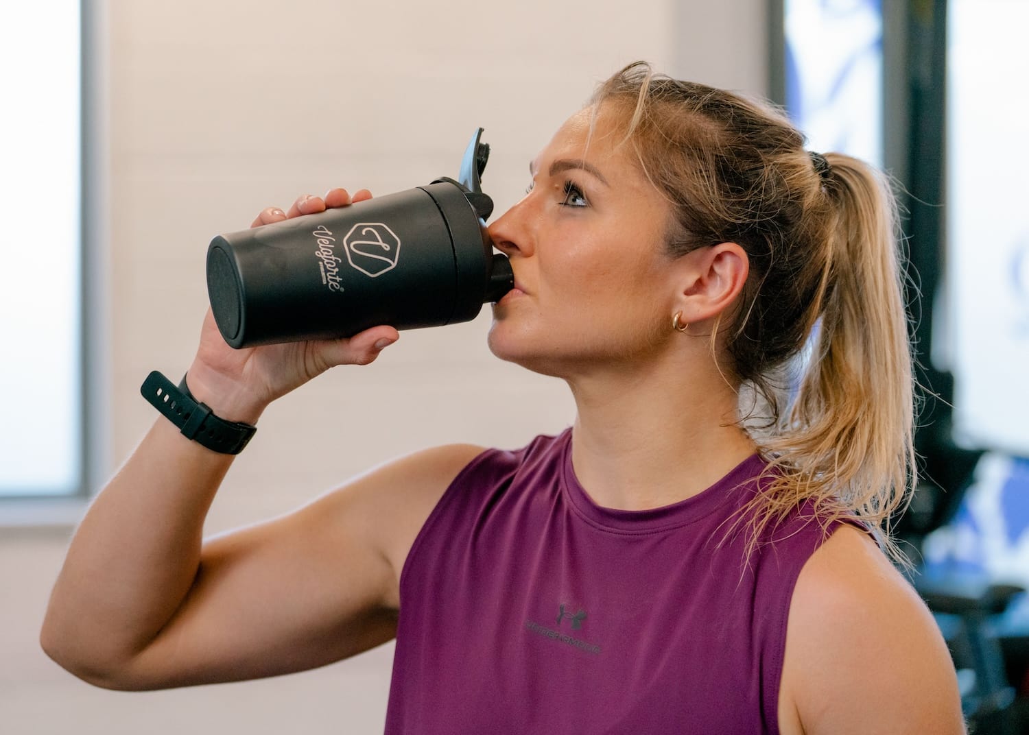 Woman in a gym drinking from a Veloforte protein shaker
