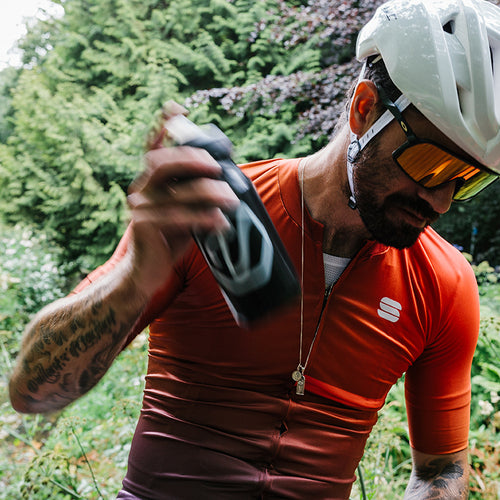 Cyclist in a helmet shaking up a Veloforte water bottle