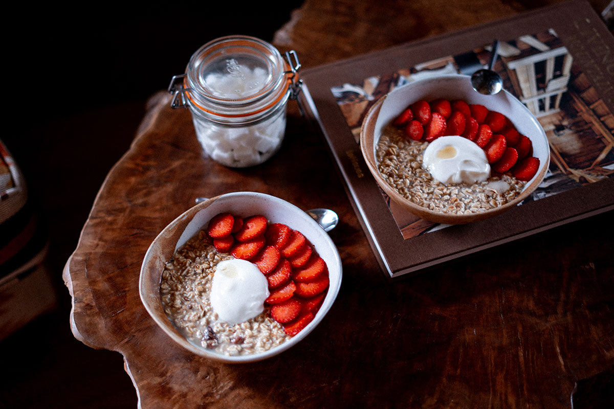 Two bowls of overnight oats with strawberries and yoghurt on a wooden table.
