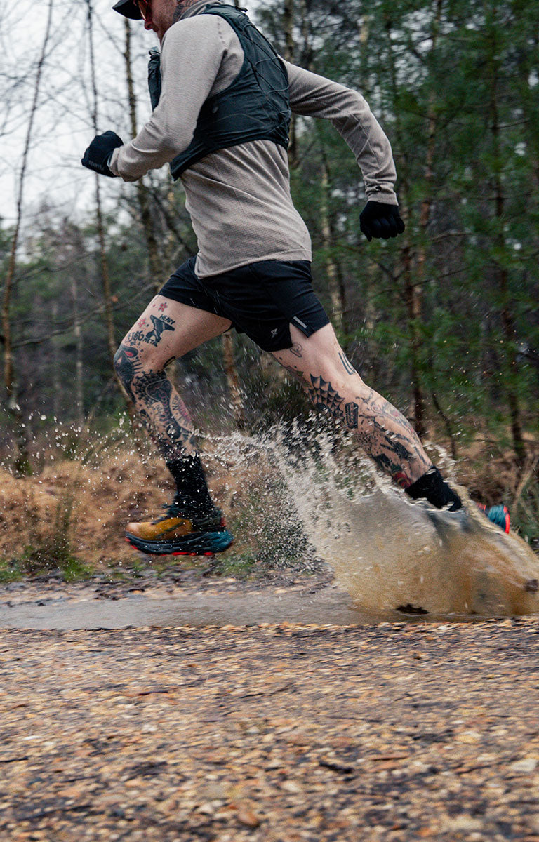 Person running through a puddle on a forest trail