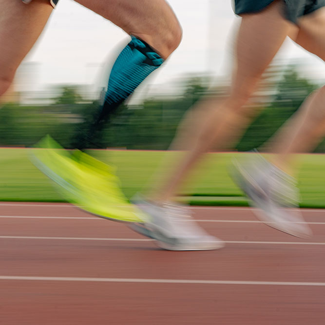 Blurred motion of runners on a track with green grass and trees in the background