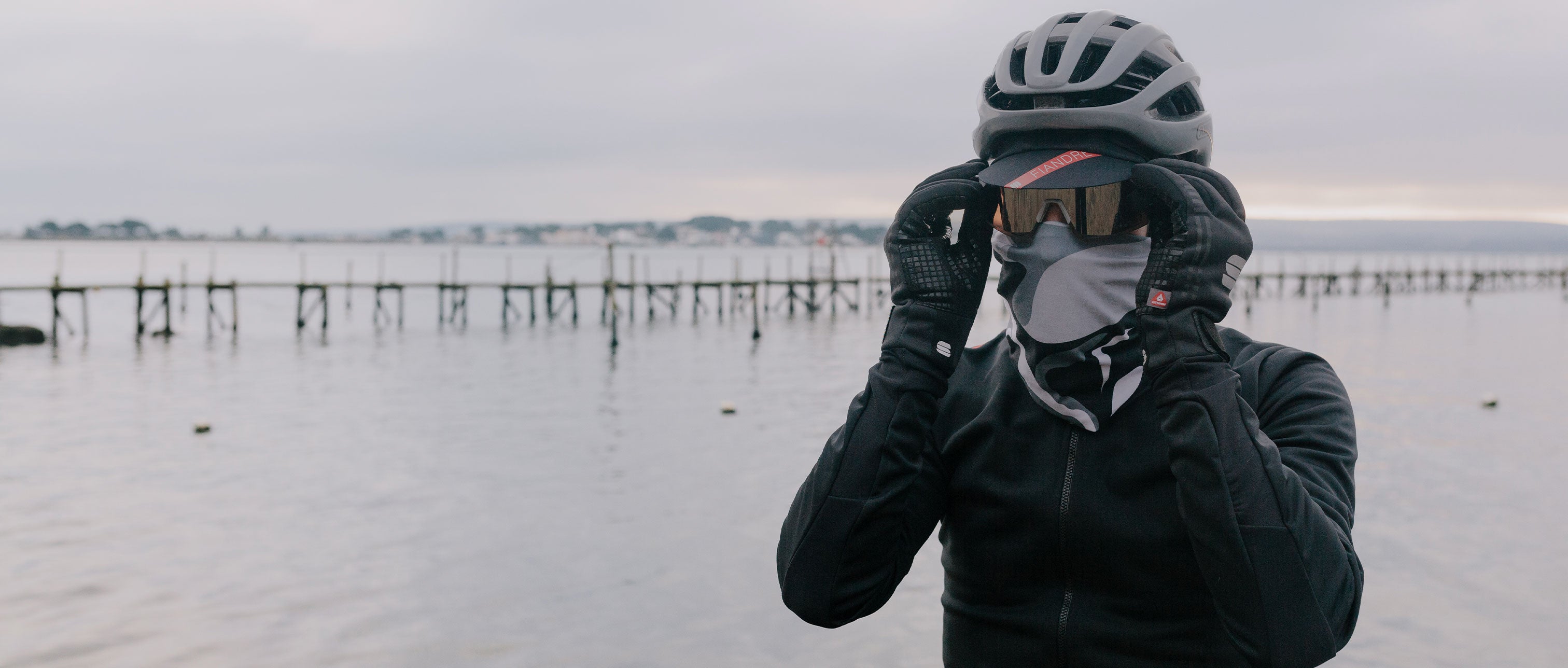 Person wearing a helmet and dark jacket by a waterfront on an overcast day